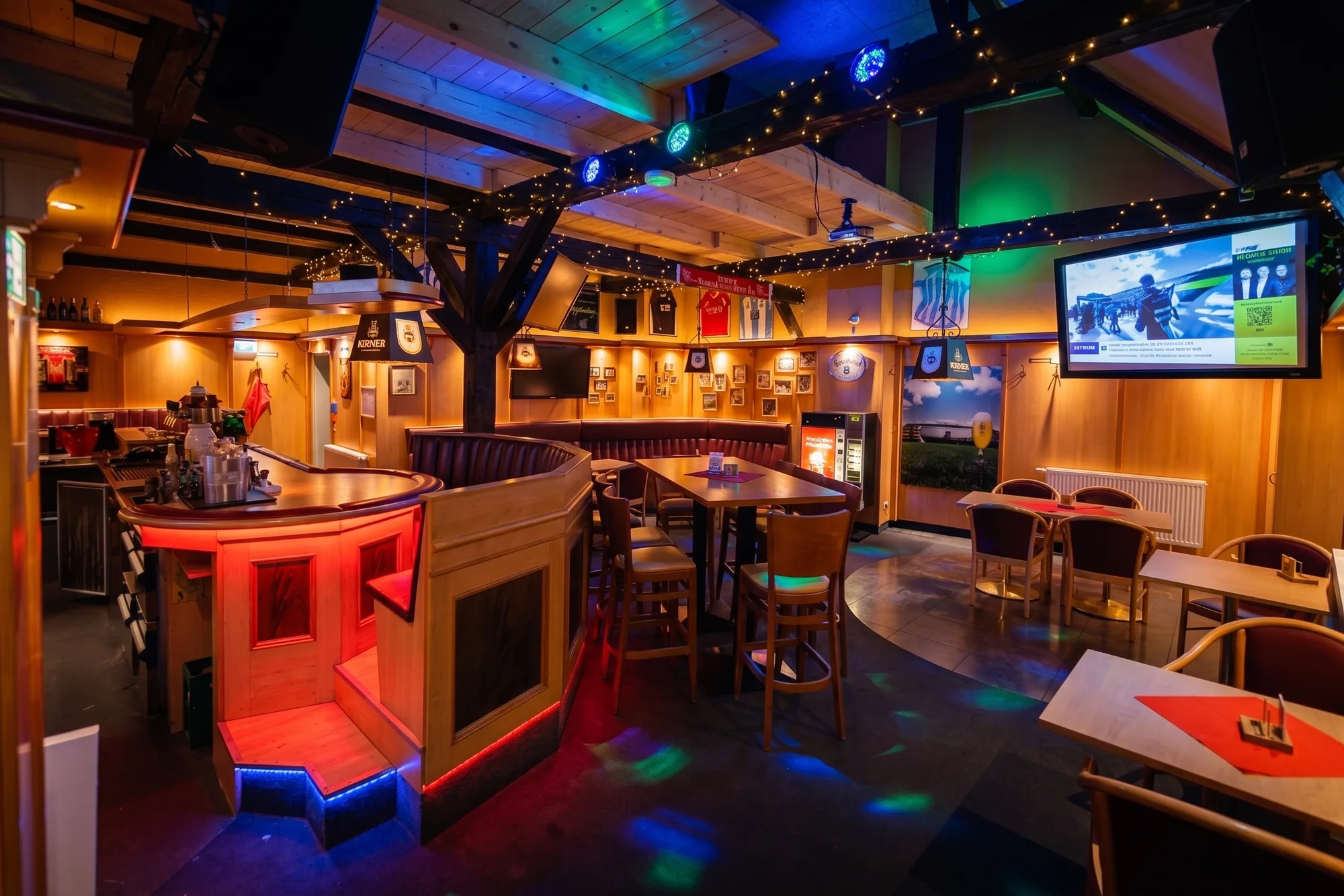 Holztheke und Sitzgruppen in der Sportsbar des Brauhauses unter farbig beleuchteten Deckenbalken