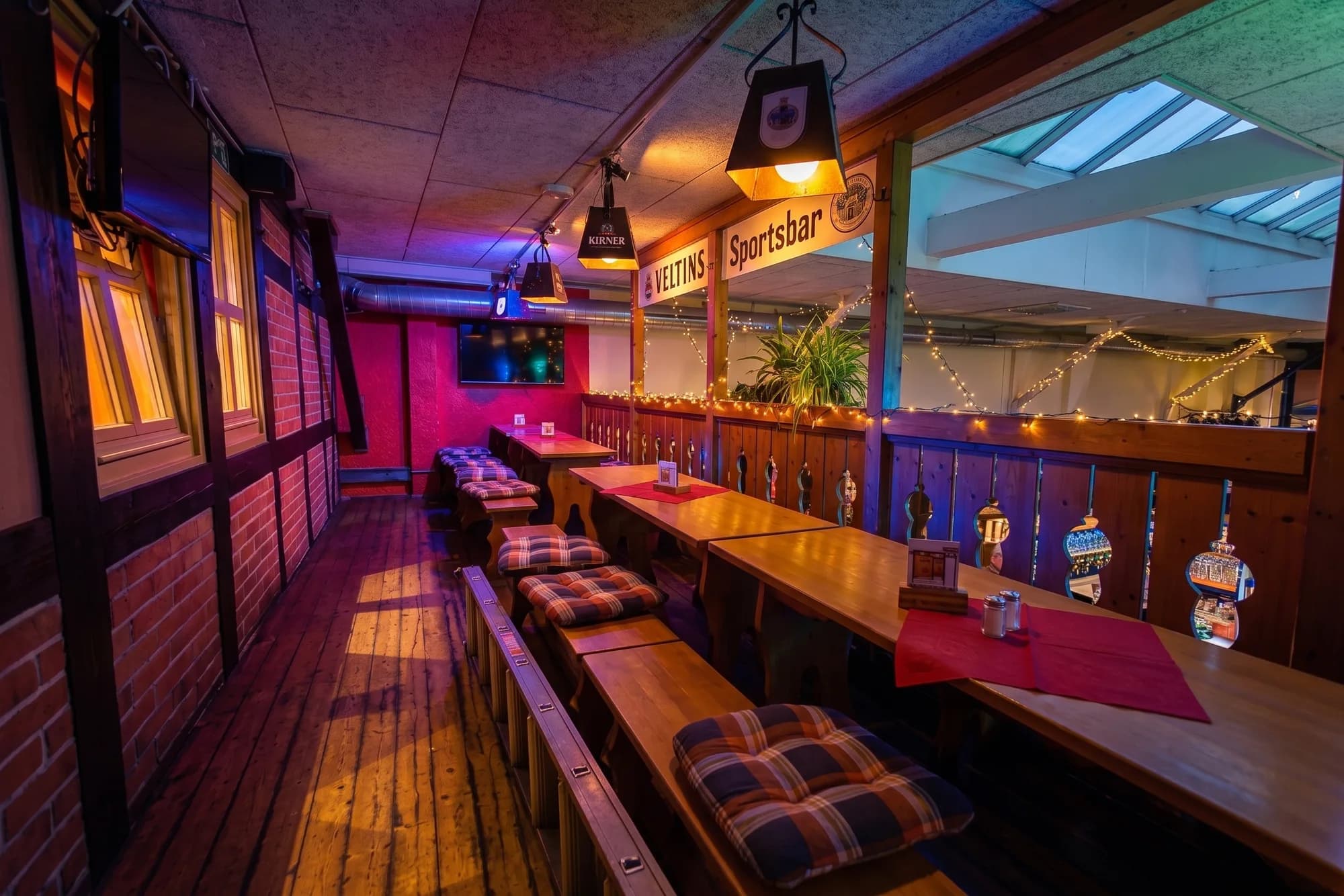 Gepolsterte Bänke und Holztische entlang der farbig beleuchteten Galerie an der Sportsbar