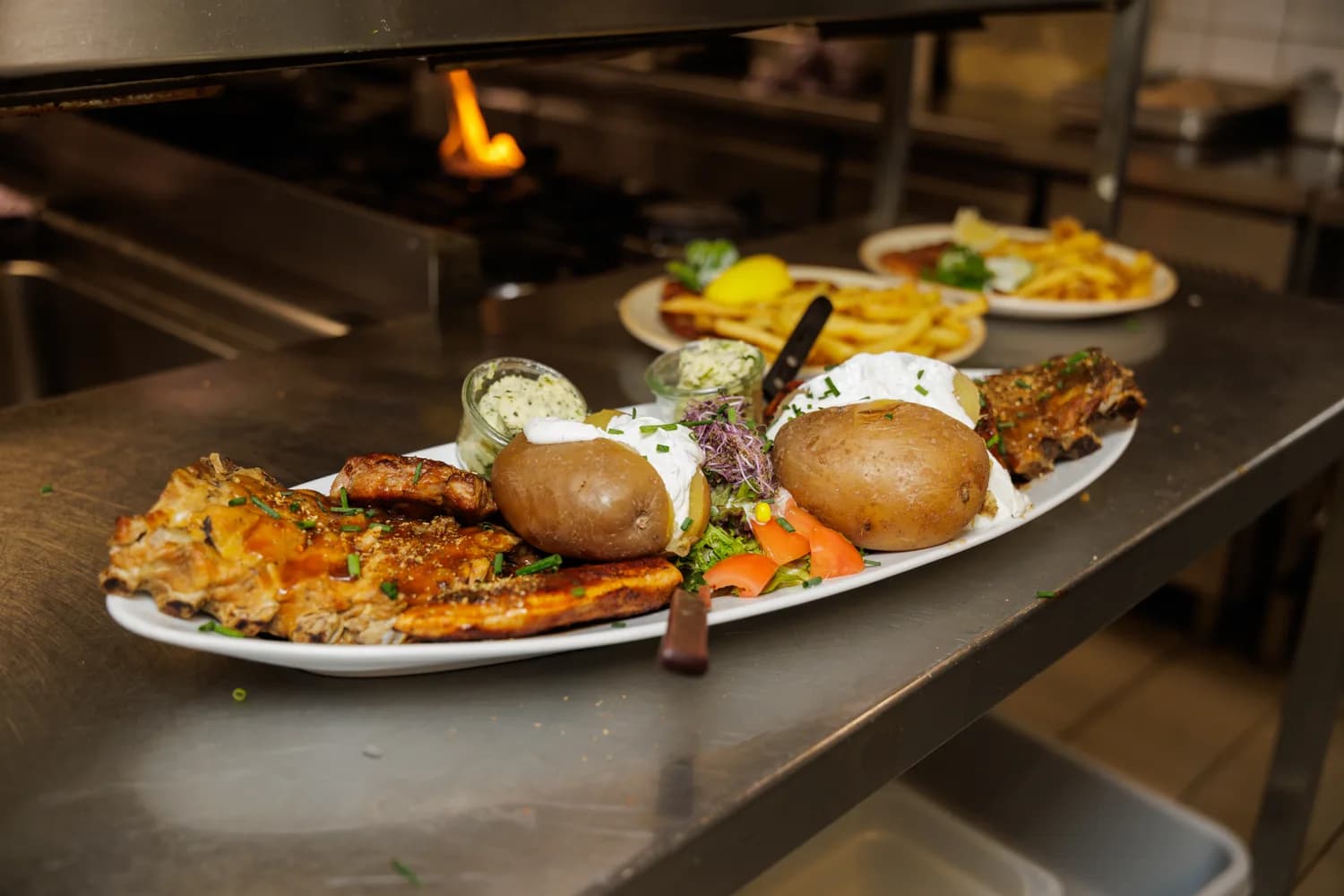 Große Grillplatte mit gegrilltem Fleisch, zwei Ofenkartoffeln mit Quark, Kräuterbutter und Salat in der Brauhausküche